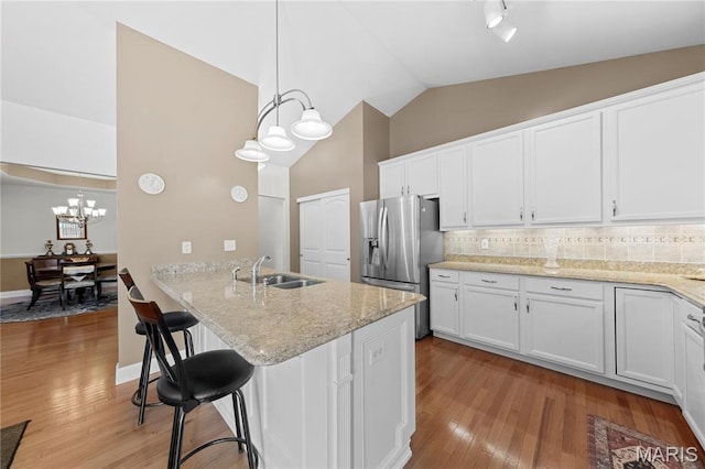kitchen featuring stainless steel refrigerator with ice dispenser, a chandelier, white cabinets, a sink, and decorative backsplash
