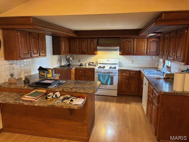 kitchen with white gas range oven, a sink, light wood-type flooring, under cabinet range hood, and tasteful backsplash