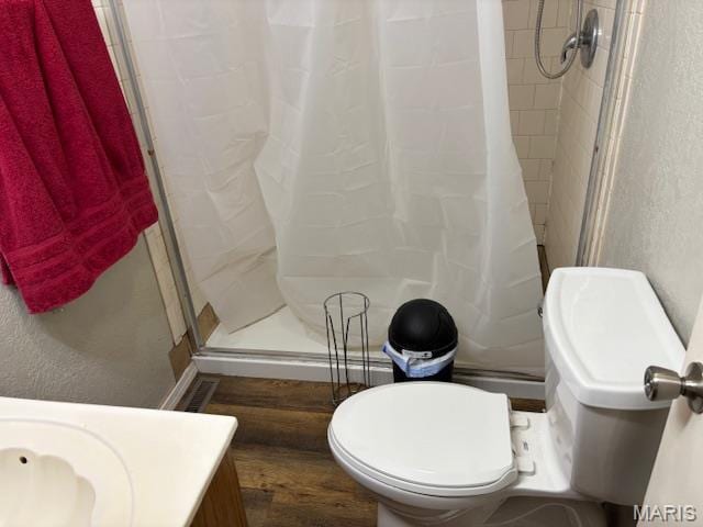 bathroom featuring wood finished floors, a stall shower, toilet, and vanity