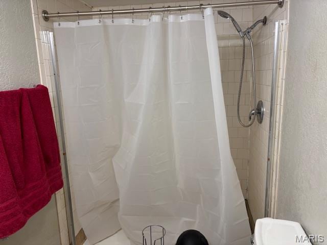 bathroom featuring tiled shower and a textured wall