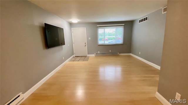 empty room featuring baseboard heating, a baseboard heating unit, light wood-style flooring, and baseboards