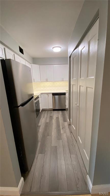 kitchen with appliances with stainless steel finishes, wood finished floors, white cabinets, light countertops, and backsplash