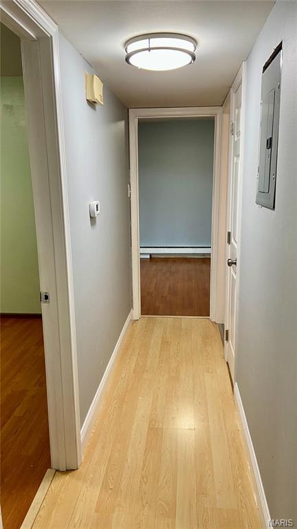 corridor with electric panel, wood finished floors, baseboard heating, and baseboards