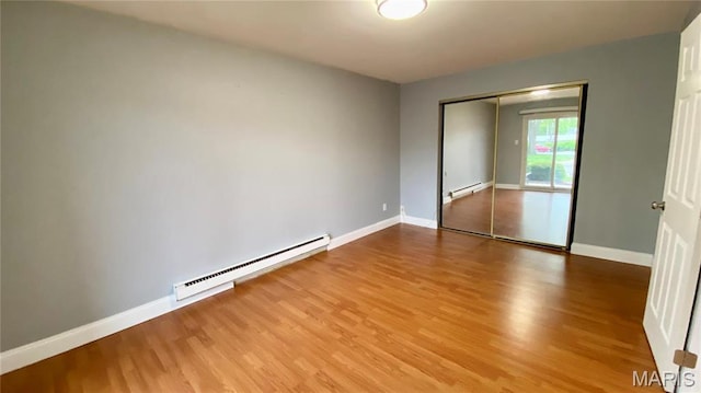 unfurnished bedroom featuring baseboard heating, a baseboard heating unit, wood finished floors, and baseboards