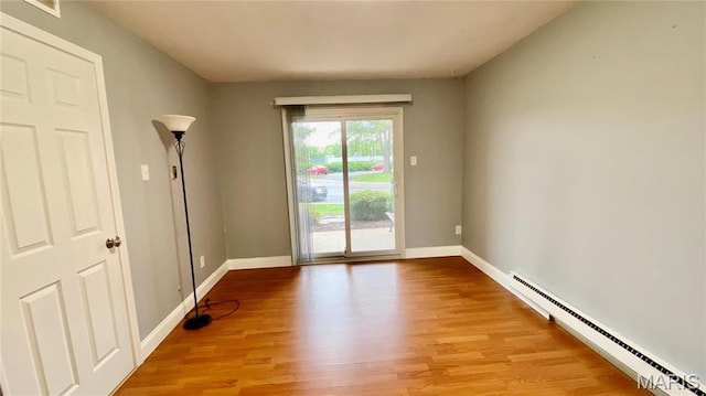 unfurnished room featuring a baseboard heating unit, light wood-style flooring, and baseboards