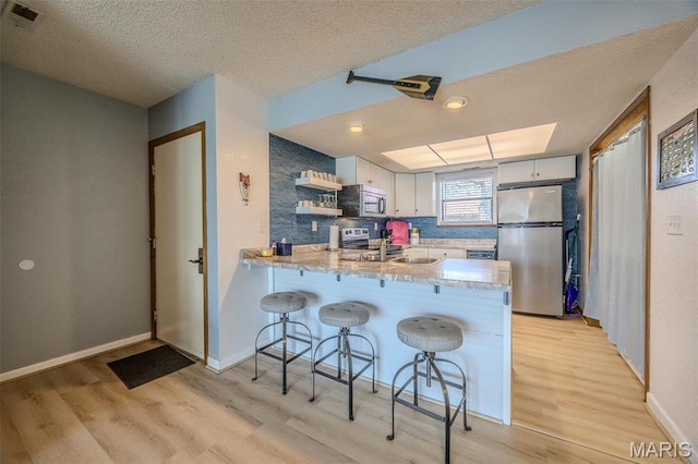256 Lone Oak Unit 15, Sunrise Beach, MO 65079 - kitchen with stainless steel appliances, light wood-type flooring, a peninsula, a textured ceiling, and open shelves