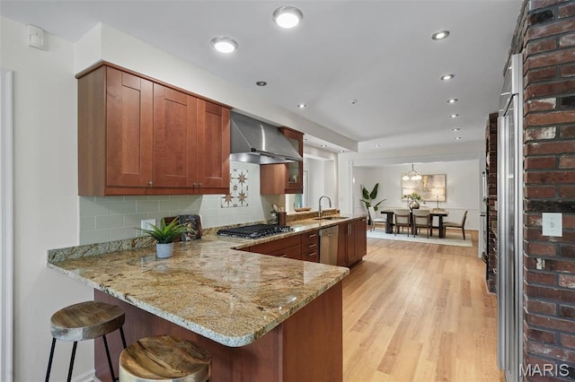 2125 Crystal Dr, Saint Louis, MO 63131 - kitchen with wall chimney range hood, a peninsula, a sink, light wood-type flooring, and stainless steel appliances