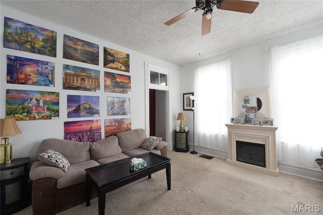carpeted living area featuring a textured ceiling, a ceiling fan, and a glass covered fireplace