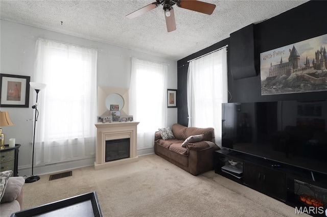 carpeted living area featuring a glass covered fireplace, a ceiling fan, and a textured ceiling