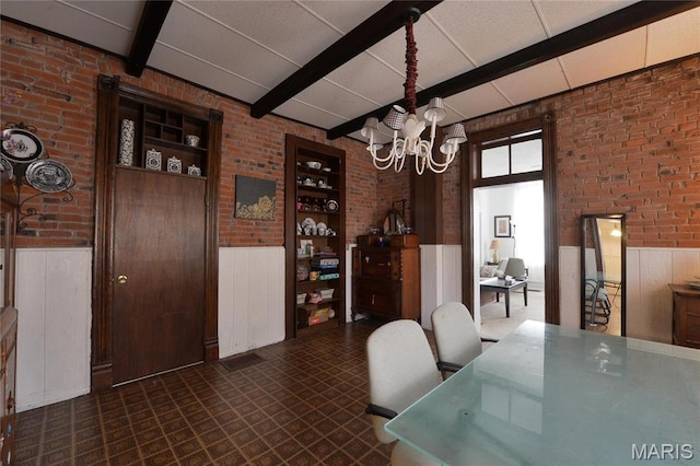 dining area featuring brick wall, a chandelier, beam ceiling, wainscoting, and dark flooring