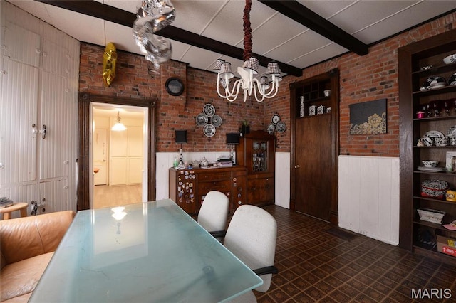 dining room featuring a chandelier, beam ceiling, brick wall, a wainscoted wall, and dark floors