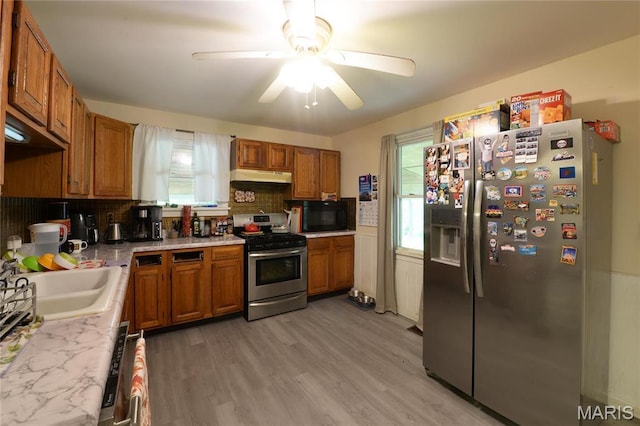 kitchen with stainless steel appliances, under cabinet range hood, brown cabinets, and healthy amount of natural light