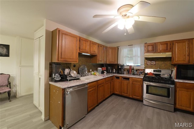 kitchen featuring stainless steel appliances, under cabinet range hood, light countertops, light wood-style flooring, and brown cabinets