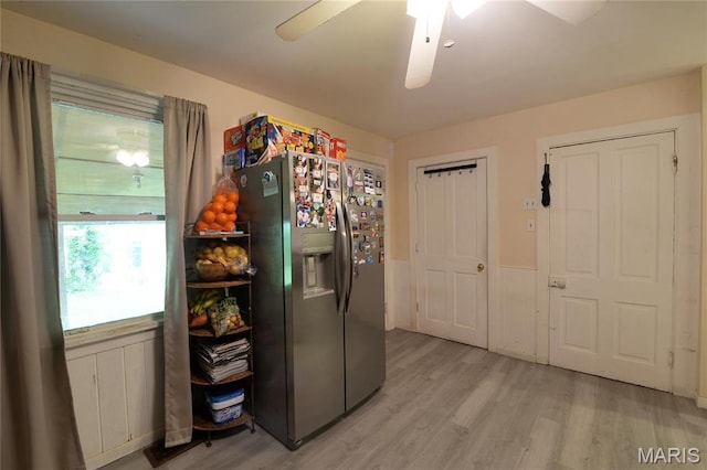 kitchen with stainless steel fridge with ice dispenser, light wood-type flooring, a ceiling fan, and a wainscoted wall