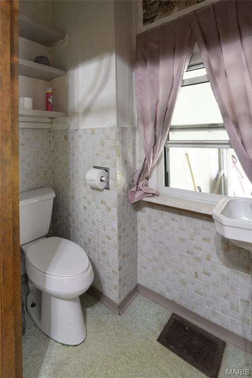 bathroom with toilet, tile patterned floors, and tile walls