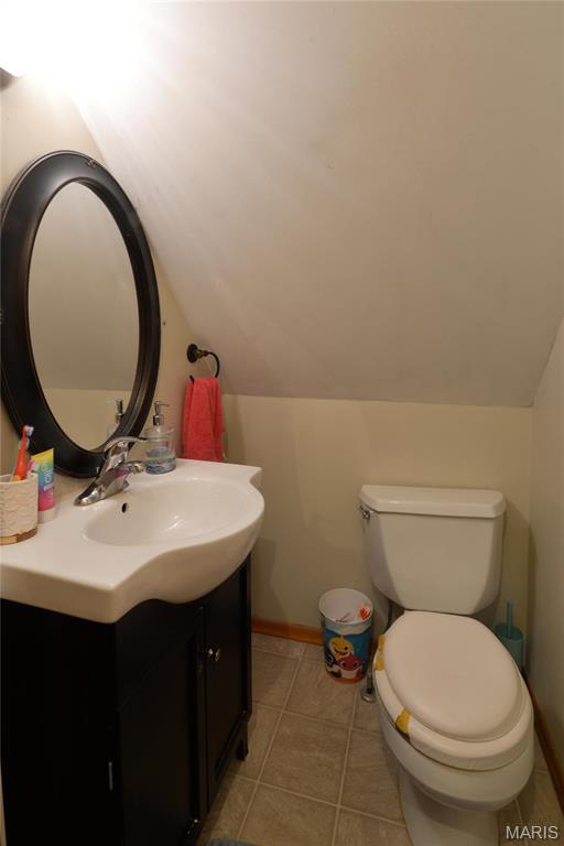 bathroom with lofted ceiling, vanity, toilet, tile patterned flooring, and baseboards