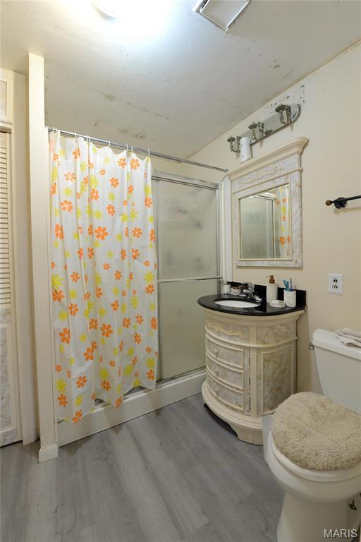 bathroom featuring wood finished floors, a stall shower, toilet, and vanity