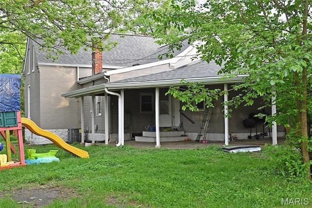 back of house featuring roof with shingles, entry steps, a sunroom, a playground, and a yard
