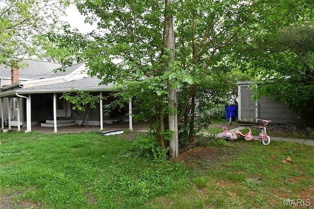 view of grassy yard with a shed, an outbuilding, and a patio area