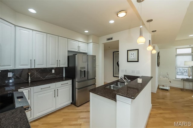 kitchen with a sink, stainless steel fridge, light wood-type flooring, tasteful backsplash, and white cabinetry