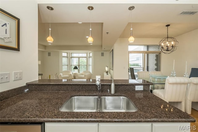 kitchen featuring open floor plan, a sink, dark stone countertops, and white cabinetry