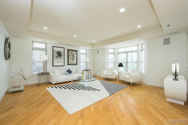 living area featuring a raised ceiling, light wood-type flooring, baseboards, and recessed lighting