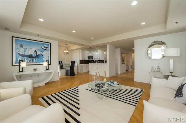 living room with a raised ceiling, light wood finished floors, recessed lighting, and baseboards