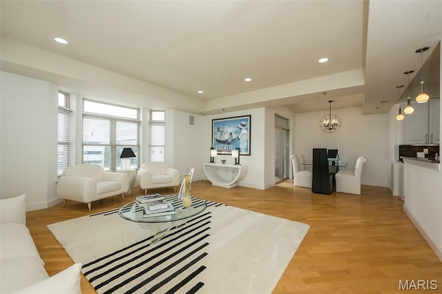 living area featuring a chandelier, light wood finished floors, baseboards, a tray ceiling, and recessed lighting
