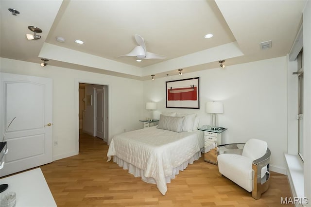 bedroom with a tray ceiling, baseboards, light wood finished floors, recessed lighting, and a ceiling fan
