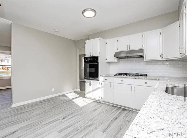 5108 S Gem Dr, High Ridge, MO 63049 - kitchen with black oven, under cabinet range hood, stainless steel gas stovetop, light wood-type flooring, and tasteful backsplash