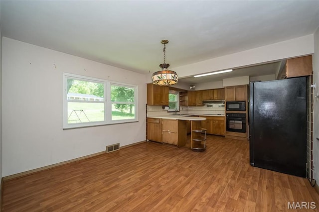 kitchen featuring black appliances, a peninsula, brown cabinets, light countertops, and light wood finished floors