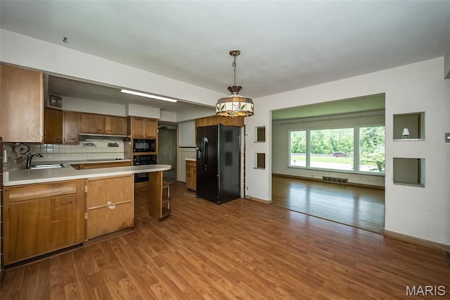 kitchen featuring black appliances, a sink, a peninsula, wood finished floors, and brown cabinets