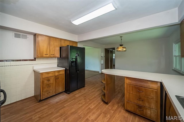 kitchen featuring black fridge, brown cabinets, light wood-type flooring, light countertops, and pendant lighting