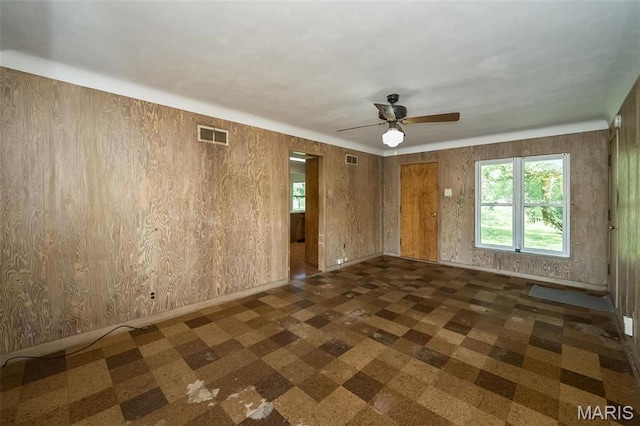 spare room featuring a ceiling fan, wooden walls, and baseboards