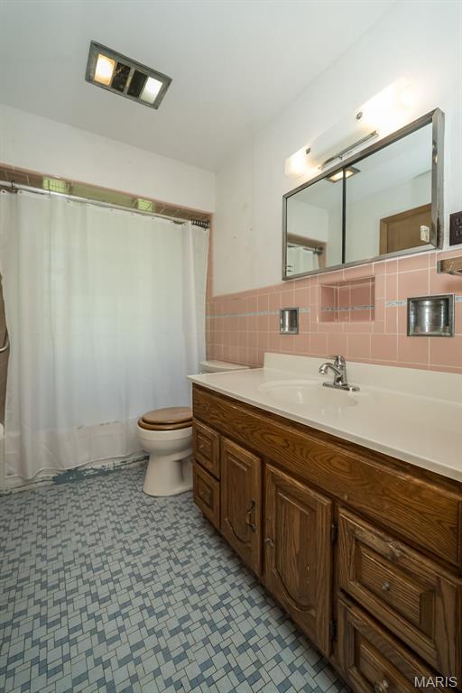 bathroom with toilet, tile patterned floors, vanity, tile walls, and shower / tub combo