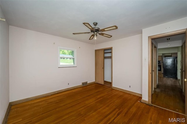unfurnished bedroom featuring freestanding refrigerator, wood finished floors, baseboards, a closet, and ceiling fan