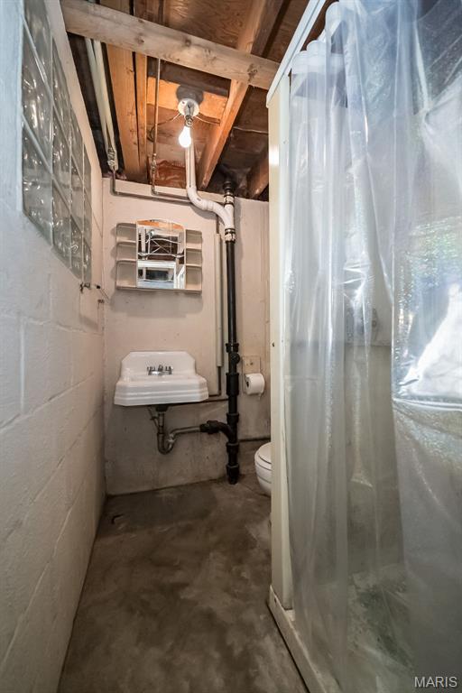 bathroom with concrete floors, a sink, toilet, and a stall shower