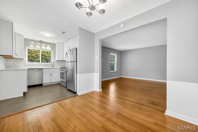 7114 Clayton Rd, Saint Louis, MO 63117 - kitchen featuring appliances with stainless steel finishes, plenty of natural light, a chandelier, white cabinets, and wainscoting