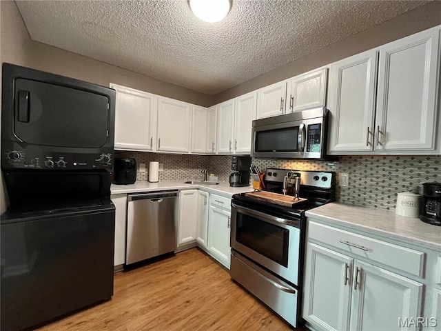 9169 N Swan Cir, Brentwood, MO 63144 - kitchen with appliances with stainless steel finishes, stacked washer / dryer, light countertops, light wood finished floors, and a textured ceiling