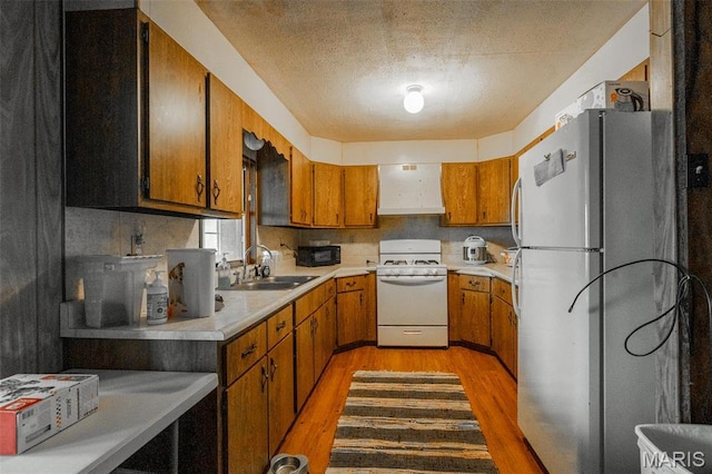 kitchen with white appliances, a sink, light wood-type flooring, brown cabinets, and a textured ceiling