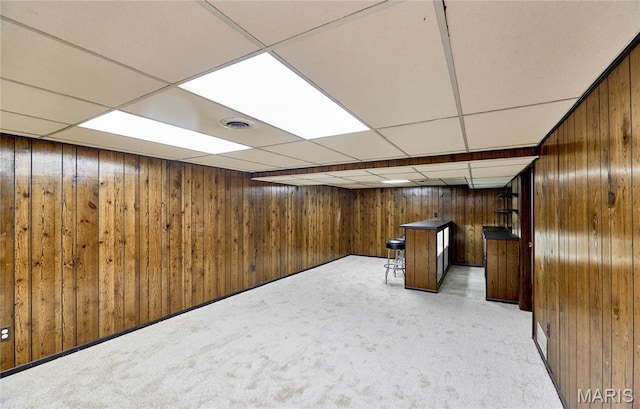 finished below grade area with wooden walls, a drop ceiling, and light carpet