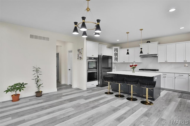 112 Westhaven View Dr, Wentzville, MO 63385 - kitchen with black appliances, light wood-style floors, light countertops, under cabinet range hood, and a breakfast bar