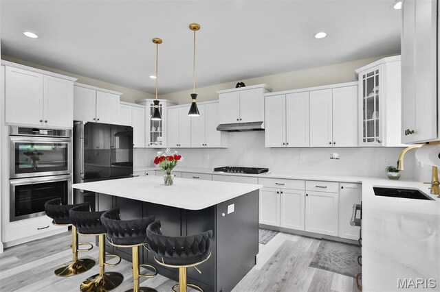 112 Westhaven View Dr, Wentzville, MO 63385 - kitchen featuring stainless steel double oven, a sink, under cabinet range hood, light wood-type flooring, and a center island