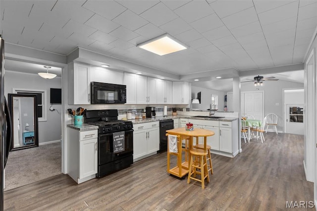 kitchen with black appliances, a peninsula, white cabinets, wood finished floors, and crown molding