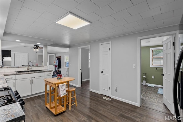 kitchen with a sink, a ceiling fan, white cabinetry, dark wood-type flooring, and range with gas cooktop