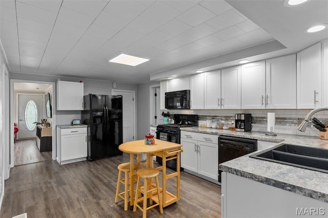 kitchen with black appliances, a sink, white cabinetry, tasteful backsplash, and dark wood-style flooring