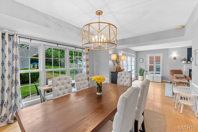 dining area with a chandelier, light wood-style flooring, baseboards, and a fireplace