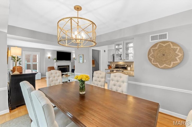 dining area featuring light wood-type flooring, a chandelier, a fireplace, and baseboards