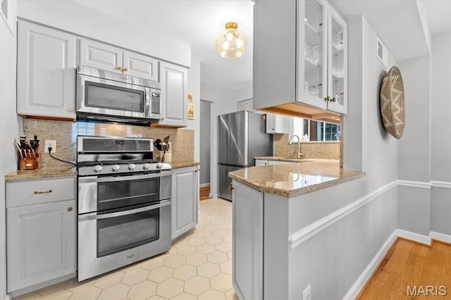kitchen with stainless steel appliances, a sink, glass insert cabinets, light stone counters, and a peninsula