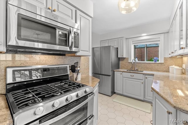 kitchen with appliances with stainless steel finishes, a sink, light tile patterned floors, decorative backsplash, and light stone counters